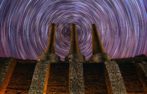 Destacado. Fotografía nocturna de larga exposición. Traza de estrellas startrail circular con 3 chimeneas de una antigua fábrica abandonada