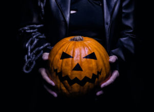 Personaje disfrazado del cuervo sostiene calabaza de Halloween