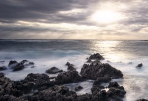 Amanecer en la costa de Menorca. Olas rompiendo contra las piedras mientras sale el sol entre las nubes