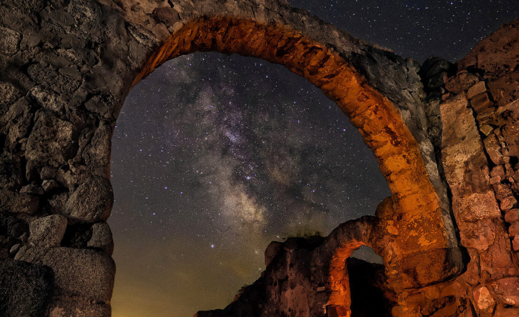 Fotografía nocturna de larga exposición de un arco de una iglesia en ruinas visigoda con la vía láctea cruzando por detrás