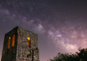 Fotografía nocturna de larga exposición de Vía láctea con una iglesia castillo en ruinas con iluminación nocturna