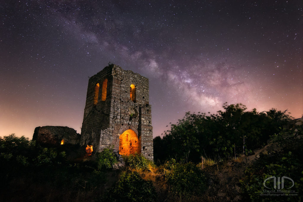 Fotografía nocturna de larga exposición de Vía láctea con una iglesia castillo en ruinas con iluminación nocturna