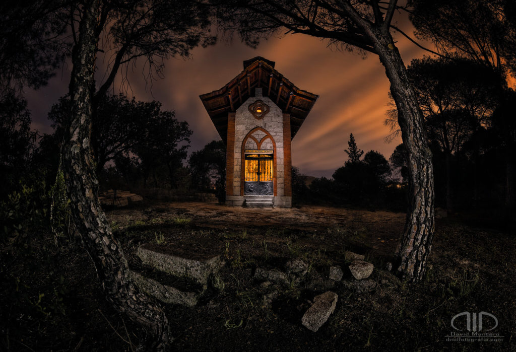 Ermita nocturna, larga exposición de esta ermita en el bosque, enmarcada por los troncos de pinos