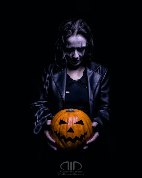 Personaje disfrazado del cuervo sostiene calabaza de Halloween